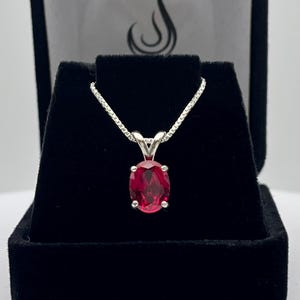 May include: A silver chain necklace with an oval-shaped red gemstone pendant.