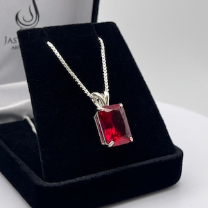 May include: A silver chain necklace with a red gemstone pendant. The gemstone is a rectangular emerald cut.