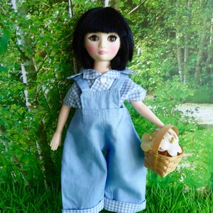 May include: A doll with black hair and blue eyes wearing a blue and white gingham dress and overalls. She is holding a basket of white flowers.