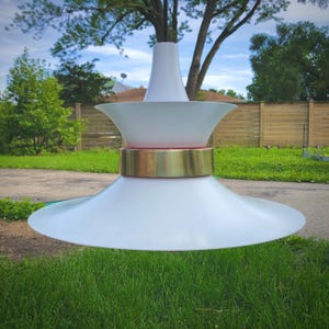 May include: A white mid-century modern pendant light fixture with a brass band and a white, slightly pink, inner shade.