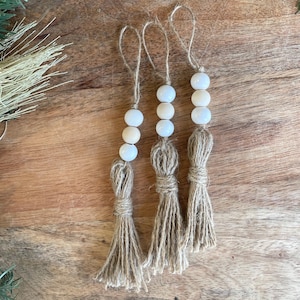 May include: Three white bead and jute tassel ornaments. The tassels are made of natural jute twine and the beads are white with a slight iridescent sheen.