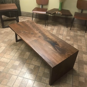 May include: A large, dark wood coffee table with a live edge top and a metal frame. The table is sitting on a tiled floor.