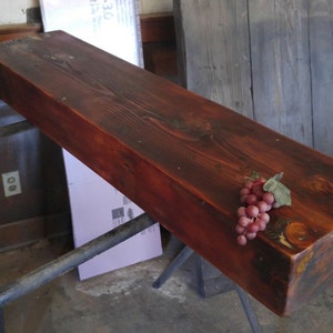 May include: A dark red wooden shelf with a cluster of red grapes on top. The shelf is made of reclaimed wood and has a rustic look.