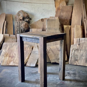 May include: A dark brown wooden table with a rectangular top and four legs. The table is standing on a concrete floor in front of a wall with wooden planks.