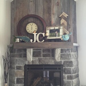May include: A stone fireplace with a black metal surround and a wood-burning fire. The fireplace is decorated with a wooden mantel, a clock, a picture frame, and wooden letters spelling "JC".