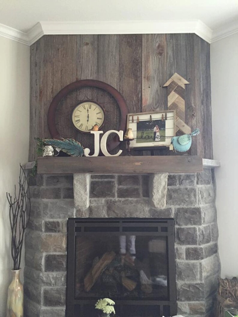 May include: A stone fireplace with a black metal surround and a wood-burning fire. The fireplace is decorated with a wooden mantel, a clock, a picture frame, and wooden letters spelling "JC".