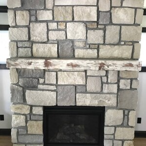 May include: A fireplace with a stone surround and a black metal firebox. The stone is a light gray color with some brown and beige tones. The mantel is made of wood and has a distressed white finish.
