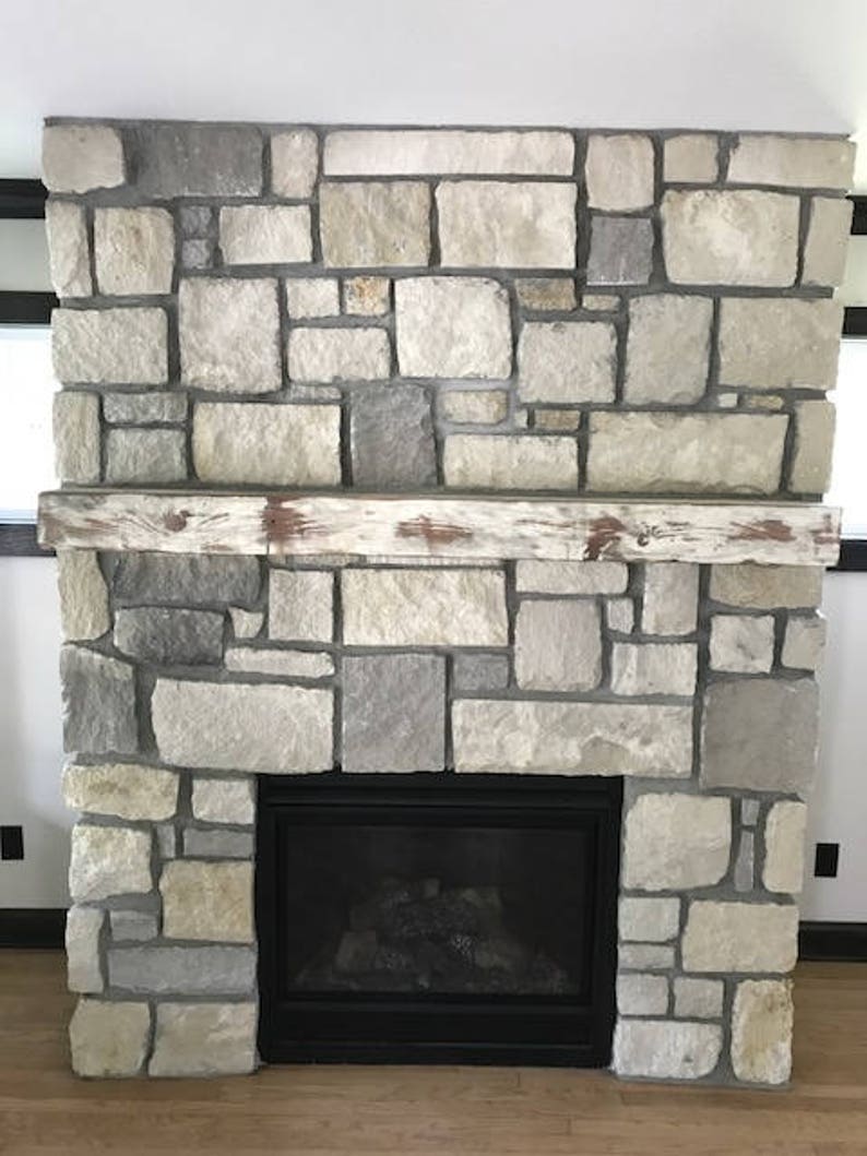 May include: A fireplace with a stone surround and a black metal firebox. The stone is a light gray color with some brown and beige tones. The mantel is made of wood and has a distressed white finish.