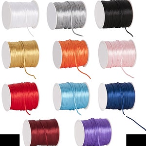 May include: Twelve spools of satin ribbon in various colors, including white, silver, black, gold, orange, pink, red, light blue, navy blue, burgundy, and lavender.