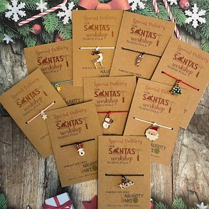 May include: A collection of eight Christmas bracelets with different charms, each with a tag that reads "Special Delivery from Santa's Workshop North Pole". The charms include a reindeer, a candy cane, a Christmas tree, a snowman, a Santa Claus, and a bell. The tags also have the words "Naughty or Nice" and a delivery date of December 25th.