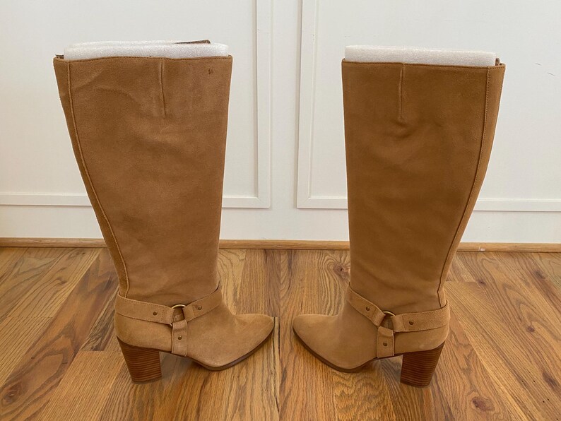 Puede incluir: Un par de botas de ante marr&oacute;n de ca&ntilde;a alta con tac&oacute;n grueso y detalle de hebilla en el eje.