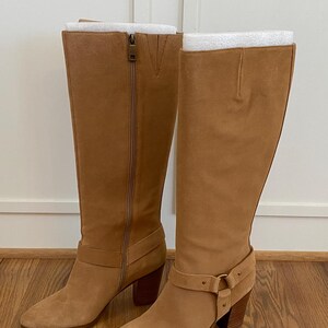 Puede incluir: Un par de botas de ca&ntilde;a alta de ante marr&oacute;n con un detalle de hebilla en el eje y un tac&oacute;n de bloque.