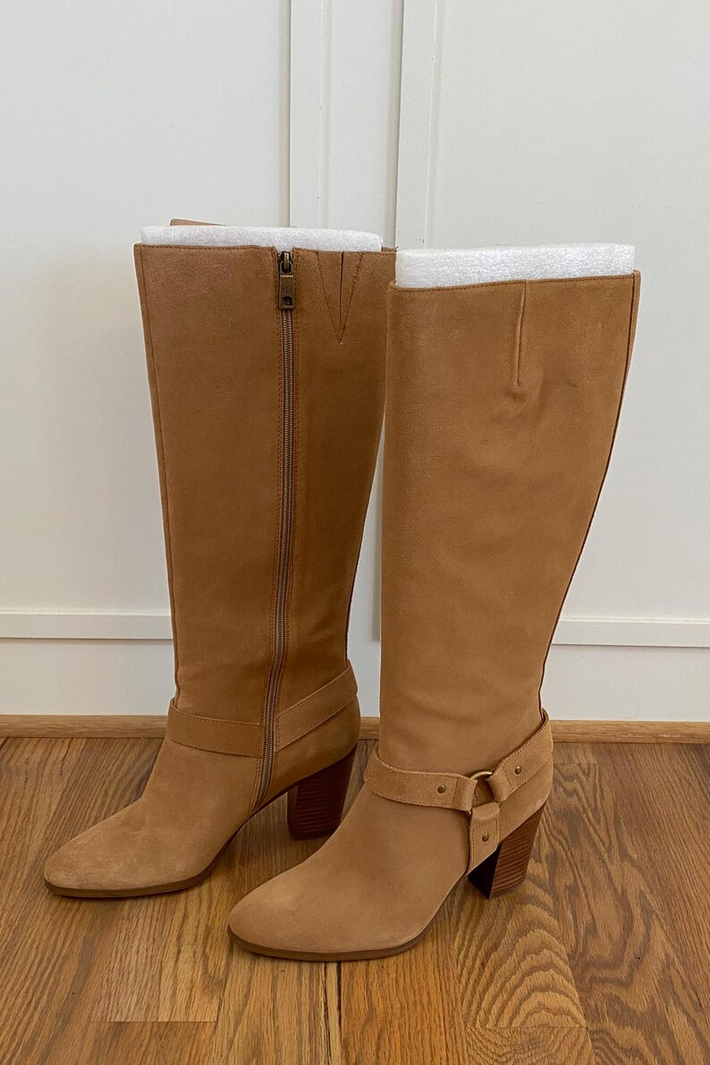 Puede incluir: Un par de botas de ca&ntilde;a alta de ante marr&oacute;n con un detalle de hebilla en el eje y un tac&oacute;n de bloque.