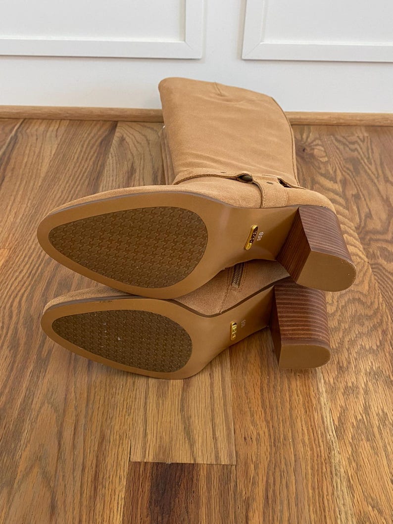 Puede incluir: Un par de botas de ca&ntilde;a alta de ante marr&oacute;n con tac&oacute;n de bloque y cremallera en el interior de la bota. Las botas tienen una tira decorativa con tachuelas doradas en la parte superior del pie.