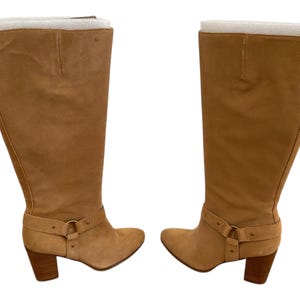 Puede incluir: Un par de botas de ante beige de ca&ntilde;a alta con tac&oacute;n de bloque y detalle de hebilla en el tobillo.