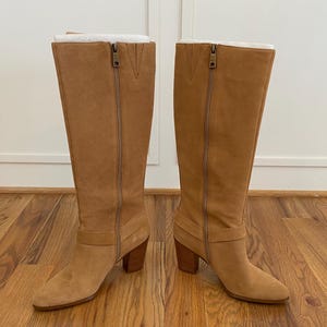 Puede incluir: Un par de botas de gamuza marr&oacute;n de ca&ntilde;a alta con tac&oacute;n de bloque y cremallera en la parte posterior. Las botas tienen un detalle de hebilla en el lateral.