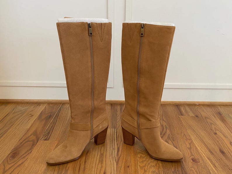 Puede incluir: Un par de botas de gamuza marr&oacute;n de ca&ntilde;a alta con tac&oacute;n de bloque y cremallera en la parte posterior. Las botas tienen un detalle de hebilla en el lateral.