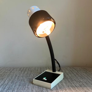 May include: A black and white desk lamp with a white shade and a black base. The lamp has a flexible arm and a switch on the base.