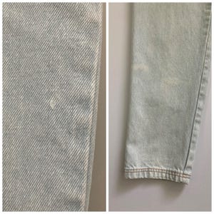 May include: Close-up of light blue denim jeans. The fabric shows a subtle texture with a small imperfection. The hem is finished with brown stitching. The jeans appear to be pre-worn.