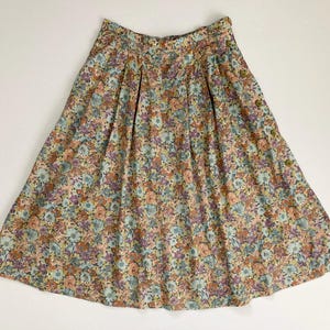 Puede incluir: Falda con estampado floral en tonos melocot&oacute;n, azul y morado. La falda tiene cintura alta, pliegues y detalles de botones. La tela es ligera y fluida, ideal para un atuendo de primavera o verano.