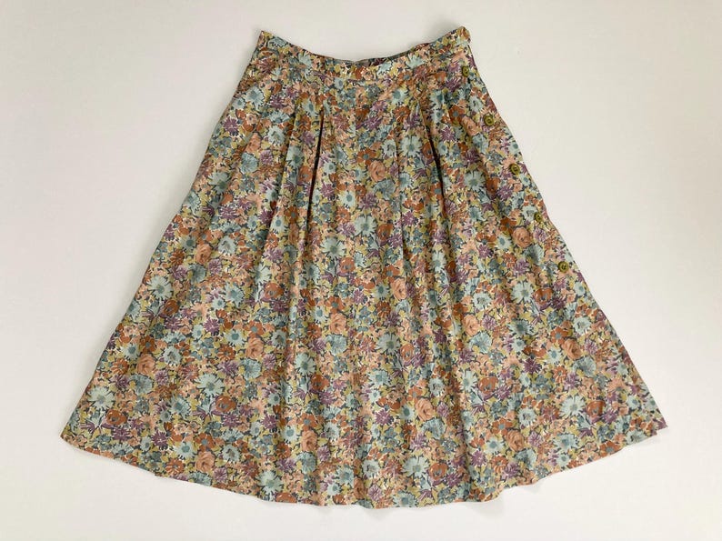 Puede incluir: Falda con estampado floral en tonos melocot&oacute;n, azul y morado. La falda tiene cintura alta, pliegues y detalles de botones. La tela es ligera y fluida, ideal para un atuendo de primavera o verano.