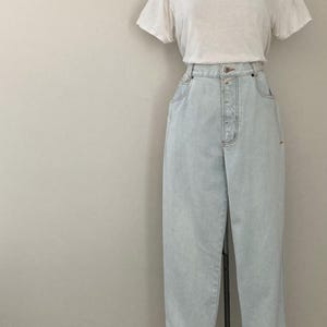 May include: A white t-shirt and light blue high-waisted jeans displayed on a mannequin. The jeans have a button fly and cuffed hems. The outfit is presented against a neutral background.