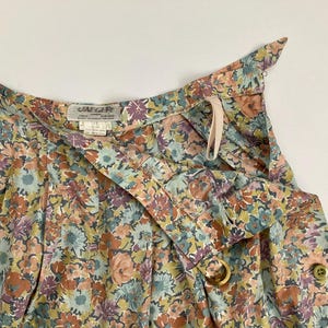 Puede incluir: Primer plano de una falda con estampado floral con dise&ntilde;o envolvente. La falda presenta una mezcla de colores, incluyendo flores melocot&oacute;n, azules y moradas. Tiene cierre de bot&oacute;n y detalle de anillo de madera. La tela parece ligera.
