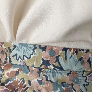 Puede incluir: Primer plano de tela con estampado floral en tonos azules, marrones y rosas. La tela est&aacute; cosida con hilo blanco. Encima de la tela floral hay una tela de color crema.