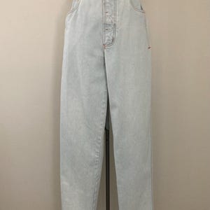 May include: Light blue denim jeans with a high waist and button fly. The jeans have a relaxed fit and a classic five-pocket design. The jeans are displayed on a mannequin.