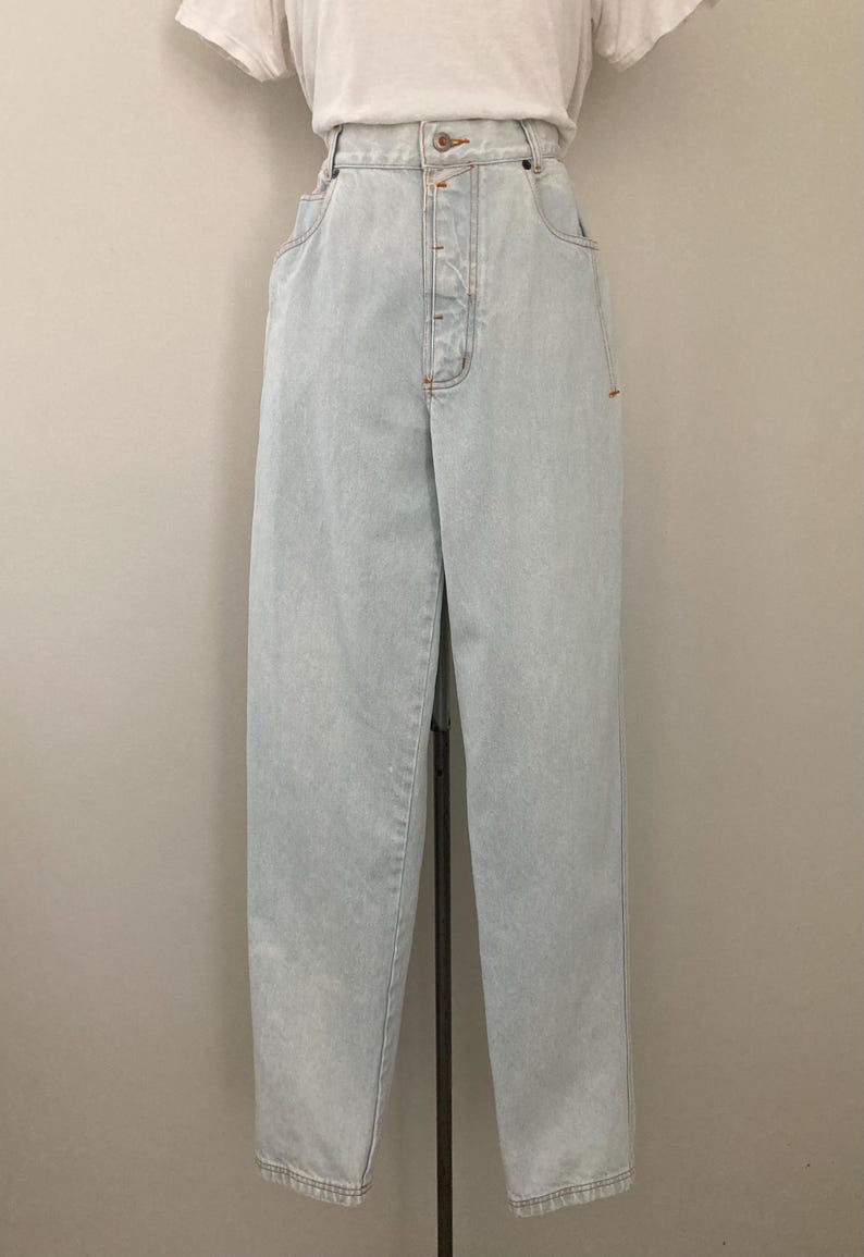 May include: Light blue denim jeans with a high waist and button fly. The jeans have a relaxed fit and a classic five-pocket design. The jeans are displayed on a mannequin.