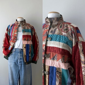 May include: A vintage patchwork jacket with a high collar and button closure. The jacket features a mix of paisley and striped patterns in red, blue, green, and beige. The jacket has a bomber style with a green ribbed hem and cuffs.