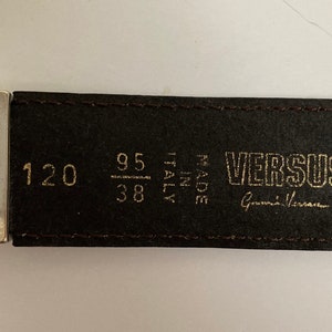 May include: A brown leather belt with the Versus logo and "Made in Italy" text. The belt measures 120 cm in length, with a 95 cm / 38 inch waist size. The buckle is silver-toned.