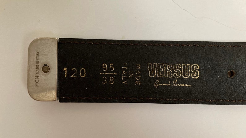 May include: A brown leather belt with the Versus logo and "Made in Italy" text. The belt measures 120 cm in length, with a 95 cm / 38 inch waist size. The buckle is silver-toned.