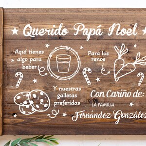 K&ouml;nnte beinhalten: Ein Holztablett mit einer wei&szlig;en Aufschrift, die "Querido Pap&aacute; Noel" lautet und eine Liste von Gegenst&auml;nden f&uuml;r den Weihnachtsmann enth&auml;lt, darunter Kekse, Milch und Karotten f&uuml;r die Rentiere. Die Aufschrift enth&auml;lt auch den Satz "Con Cari&ntilde;o de: La Familia Fern&aacute;ndez Gonz&aacute;lez".