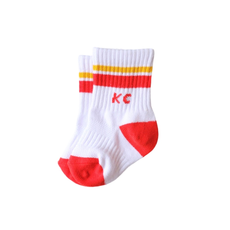 Peut inclure: Paire de chaussettes de sport blanches avec talons et orteils rouges. Les chaussettes ont des rayures rouges et jaunes en haut et les lettres "KC" en rouge. Les chaussettes sont en mati&egrave;re douce et respirante.