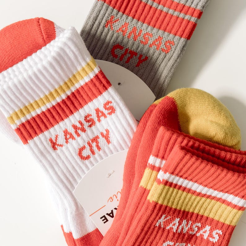 May include: Three pairs of socks with red, white, and yellow stripes. Each pair has the text "Kansas City" in red lettering.