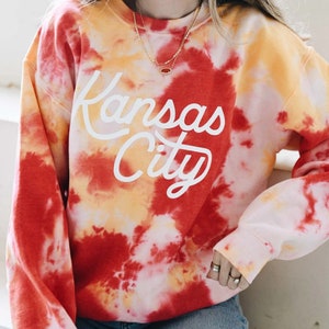 May include: Red, yellow, and white tie-dye sweatshirt with the text "Kansas City" in white script.