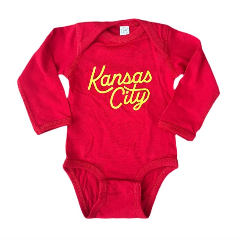 May include: Red long-sleeve baby onesie with the text "Kansas City" in yellow.