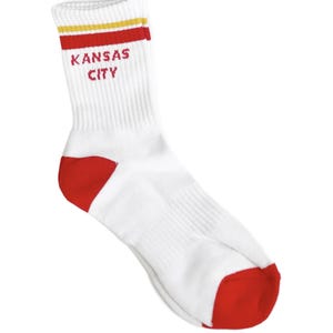 May include: White crew socks with red and yellow stripes at the top. The socks have a red heel and toe and say "Kansas City" in red letters.