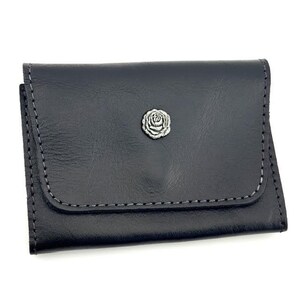 May include: A dark navy blue leather card holder featuring a rectangular flap with visible grey stitching along the edges. A small, circular silver-toned metal emblem shaped like a rose is centered on the front flap of the wallet.