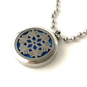May include: A silver necklace with a round pendant featuring a snowflake design. The snowflake is cut out of the metal and has a blue background.