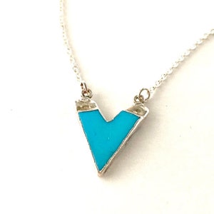 May include: A silver chain necklace with a turquoise blue V-shaped pendant.