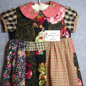 Può includere: Un vestito patchwork con colletto e maniche con stampa floreale. L'abito presenta un mix di tessuti floreali, a quadri e fantasia in vari colori, tra cui nero, rosso, verde e marrone. Ha bottoni colorati sul davanti e un'etichetta che dice "An Original handcrafted in Australia By Valma Bird."