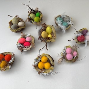 Könnte beinhalten: Neun Filznester mit bunten Filzeiern. Die Nester sind aus natürlichen Materialien gefertigt und haben ein rustikales Aussehen.