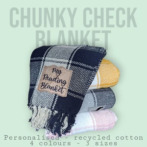 May include: A stack of four chunky check blankets in black, yellow, grey, and pink. The top blanket has a brown label that says "My Reading Blanket".