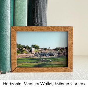 May include: A horizontal medium wallet featuring a light brown wood-grain finish and mitered corners. The front panel displays a photographic print of a park landscape with green grass, rocky terrain, a small building, and a clear blue sky.