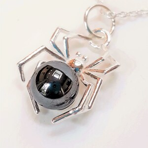 May include: A silver spider pendant featuring a black hematite gemstone. The spider has eight legs and a round body.