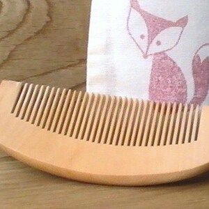 May include: A wooden comb, a bottle of beard oil labelled "Butter & Bath Beard Oil with Organic Argan Cedar & Bergamot", and a white cloth bag with a pink fox design.