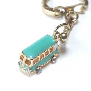 May include: A teal blue enamel bus keyring with gold trim and clear rhinestone accents. The keyring has a gold split ring.