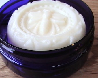 May include: A white, round, decorative soap bar with a floral design in a blue glass jar.